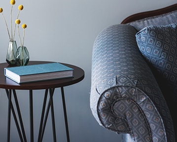 A fragment of a blue couch and a side table in front of a freshly painted light grey wall.