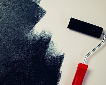 Painting over a white wall with a paint roller and black paint.